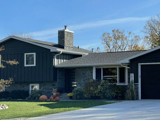 Split-level house after an exterior update, with dark vertical and horizontal siding, gray stone veneer around the entry and a stone chimney.